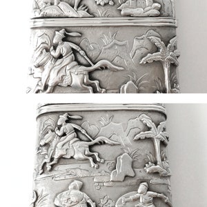 May include: A silver rectangular box with intricate embossed designs. The top and bottom sections feature scenes of people riding horses and palm trees. The middle section shows a pagoda and trees.