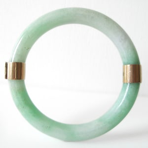 Può includere: Un braccialetto in giada verde con dettagli dorati. Il braccialetto è realizzato in giada liscia e lucida e ha un design semplice ed elegante.