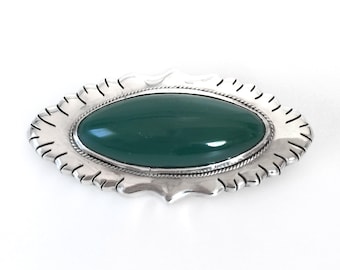 May include: A silver brooch with a green oval stone set in a decorative frame.