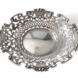 May include: A silver, openwork, decorative bowl with a round, smooth base and intricate floral designs around the rim.