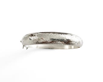 May include: A silver-toned hinged bangle bracelet featuring an engraved floral pattern across the outer surface. The bracelet has a polished metallic finish and includes a visible metal hinge and clasp mechanism on the left side of the band.