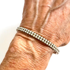 Puede incluir: Una pulsera delicada con dos filas de peque&ntilde;as cuentas blancas y redondas. La pulsera se lleva en la mu&ntilde;eca, mostrando su elegante dise&ntilde;o. Las cuentas est&aacute;n muy juntas, creando un aspecto refinado y cl&aacute;sico. Una pieza de joyer&iacute;a atemporal.