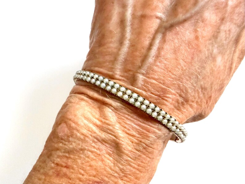 Puede incluir: Una pulsera delicada con dos filas de peque&ntilde;as cuentas blancas y redondas. La pulsera se lleva en la mu&ntilde;eca, mostrando su elegante dise&ntilde;o. Las cuentas est&aacute;n muy juntas, creando un aspecto refinado y cl&aacute;sico. Una pieza de joyer&iacute;a atemporal.