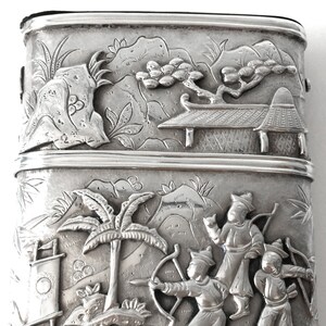 May include: A silver rectangular box with an intricate design of a Chinese landscape scene. The box is decorated with raised figures of people and trees.