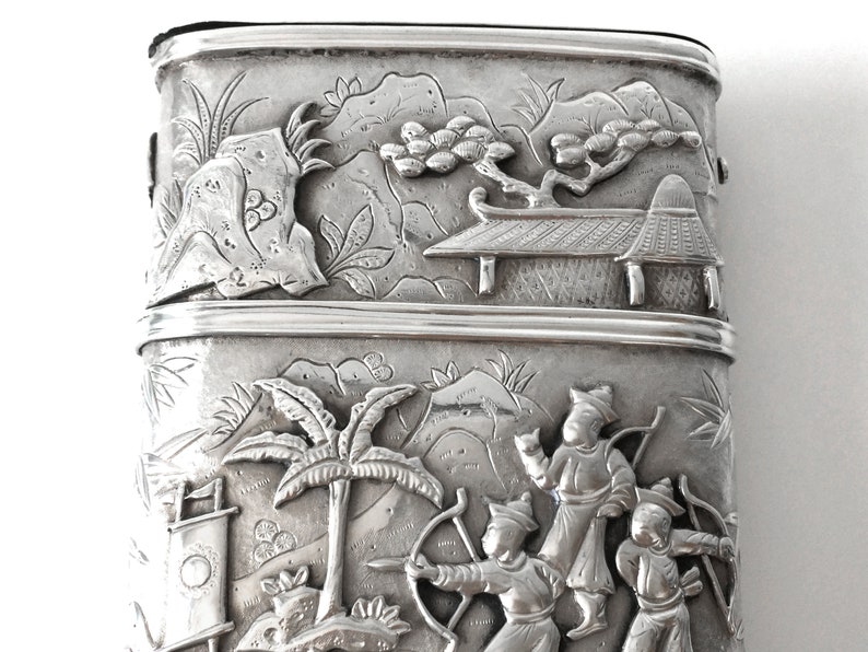 May include: A silver rectangular box with an intricate design of a Chinese landscape scene. The box is decorated with raised figures of people and trees.