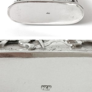 May include: Silver flask with an ornate design featuring figures and flowers. The bottom of the flask is marked with the letters "HCH".