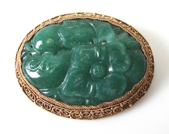 May include: A green jade flower brooch with a gold filigree border. The jade is carved in a detailed floral design.