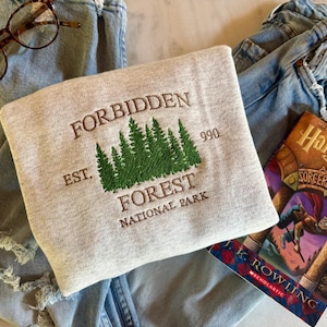 May include: A gray sweatshirt with an embroidered design that says "Forbidden Forest National Park Est. 990". The design features a row of green trees.