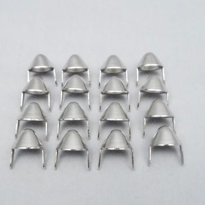 May include: A set of 18 silver-toned metal cone-shaped studs with two prongs on the bottom. The studs are arranged in rows on a white surface.