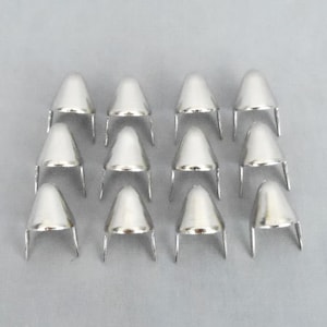 May include: A set of 12 silver-toned metal cone-shaped studs with two prongs on the bottom. The studs are arranged in a grid pattern on a gray background.