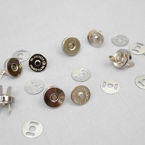 May include: A selection of silver magnetic snap fasteners for crafting. The set includes round, flat pieces with a central magnet and matching metal washers. Some pieces have the text "OK.0973628".