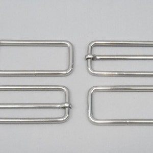 May include: Four silver metal belt buckle slides. Two of the slides have a single loop, and two have a double loop.