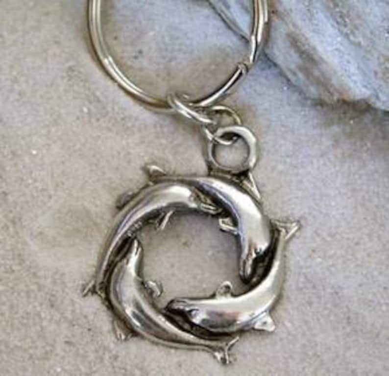 May include: Silver key chain with a circular design featuring three dolphins intertwined.