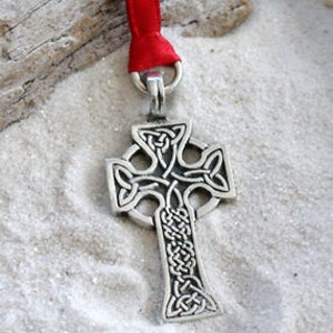 May include: A silver Celtic cross ornament with intricate knotwork design. The ornament is attached to a red ribbon.
