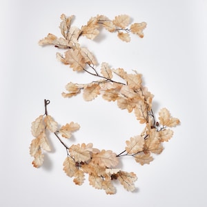 May include: A decorative garland featuring light brown oak leaves and small acorns. The leaves are arranged on dark brown stems, creating a natural and autumnal aesthetic. Perfect for fall decor, this garland adds a touch of nature to any space.