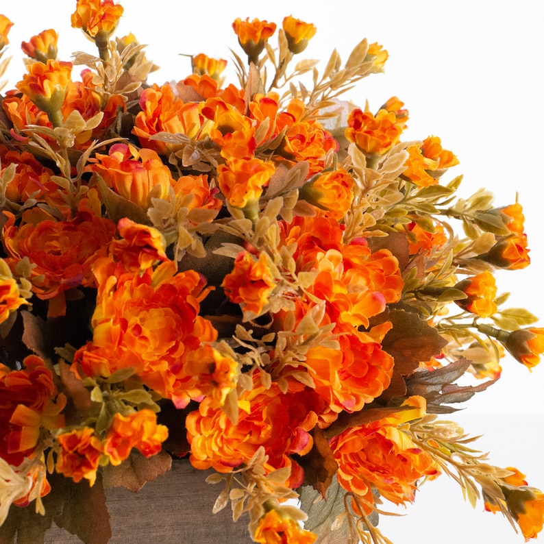 May include: A bouquet of orange silk flowers with green leaves. The flowers are arranged in a cluster and have a realistic appearance.