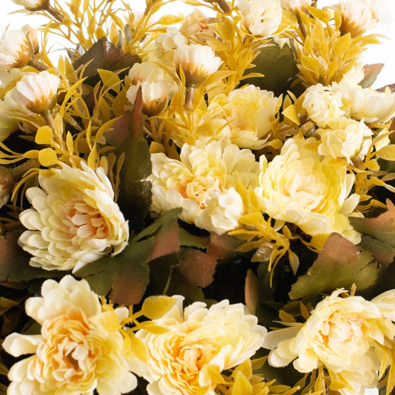 May include: A bouquet of artificial yellow chrysanthemums with green leaves and stems. The flowers are arranged in a cluster and have a realistic appearance.