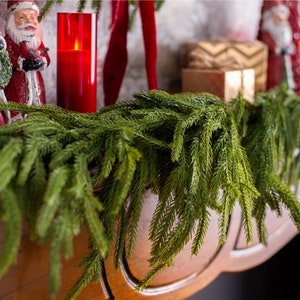 May include: A green artificial pine garland with long, thin needles, perfect for decorating a fireplace mantel or doorway for the holidays.