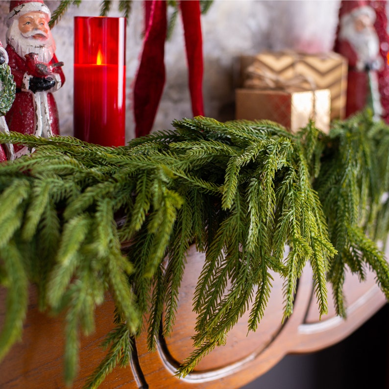May include: A green artificial pine garland with long, thin needles, perfect for decorating a fireplace mantel or doorway for the holidays.