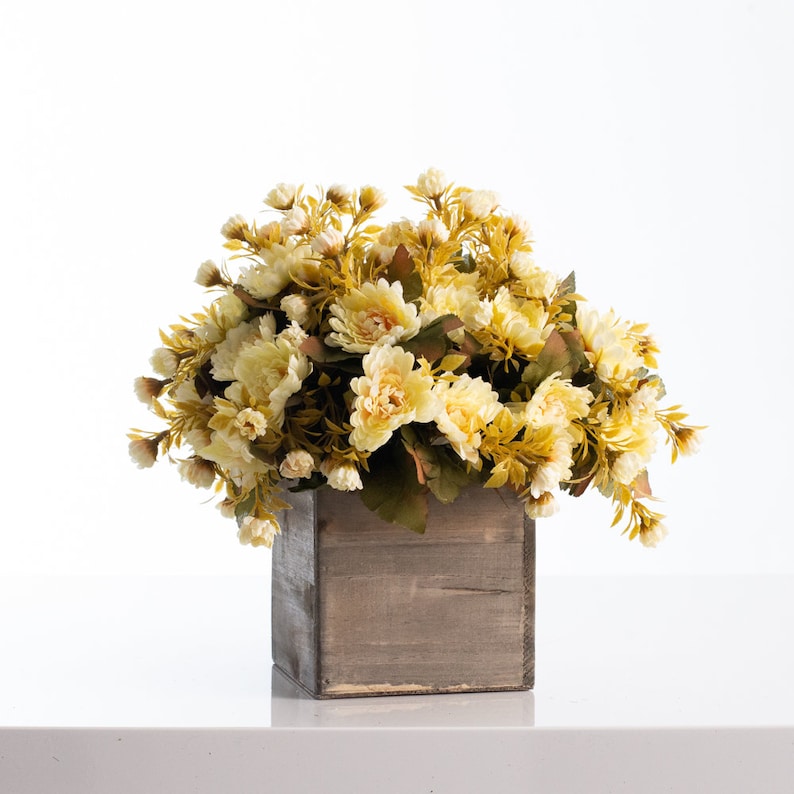 May include: A bouquet of yellow and green artificial flowers in a rustic wooden planter.