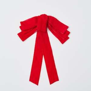 Puede incluir: Un gran lazo de terciopelo rojo con múltiples capas. El lazo está atado con dos colas largas.