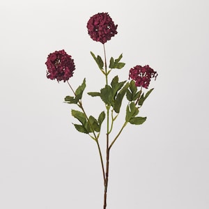 May include: A burgundy artificial flower stem with three clusters of flowers. The flowers are round and have a fluffy texture.