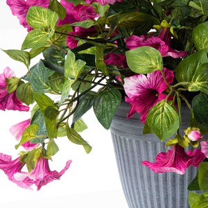 May include: A potted artificial plant with pink flowers and green leaves. The pot is gray and has a ribbed texture.
