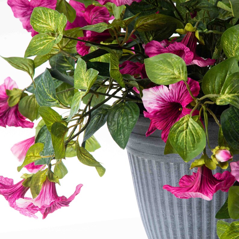 May include: A potted artificial plant with pink flowers and green leaves. The pot is gray and has a ribbed texture.