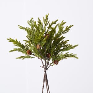 May include: A bundle of faux evergreen branches with small brown pinecones. The green foliage has a realistic texture, and the stems are tied together with a natural twine. The arrangement is set against a white background.