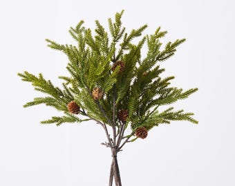 May include: A bundle of faux evergreen branches with small brown pinecones. The green foliage has a realistic texture, and the stems are tied together with natural twine. The arrangement is set against a white background.