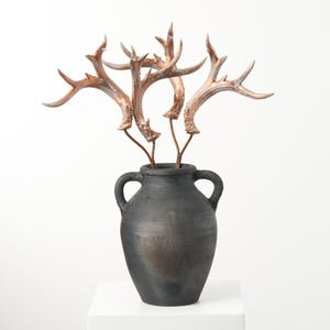 May include: A black ceramic vase with two handles, filled with a bouquet of copper-colored antlers.
