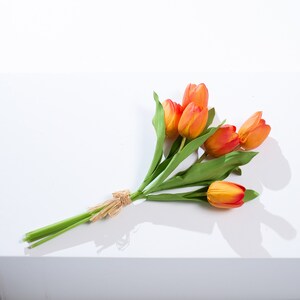 以下が含まれることがあります： 紐で結ばれたオレンジと黄色の造花チューリップのブーケです。