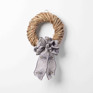May include: A natural woven straw wreath with a grey and white striped bow with a bee pattern.