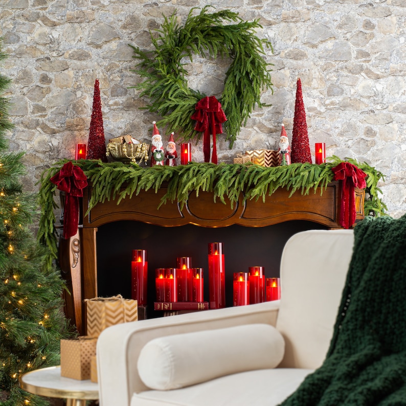 May include: A wooden fireplace mantel decorated with a green garland, red candles, and a Christmas wreath. The mantel is adorned with small figurines of Santa Claus and other holiday characters. A white couch with a green throw blanket sits in front of the fireplace.