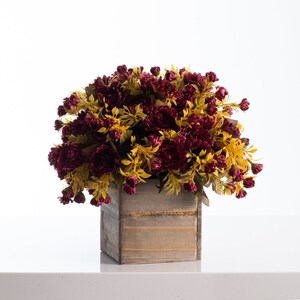 May include: A burgundy and yellow artificial flower arrangement in a wooden planter. The planter has a rustic, weathered look.