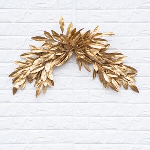 K&ouml;nnte beinhalten: Eine goldene Bl&auml;ttergirlande in Halbkreisform, perfekt, um jedem Dekor einen Hauch von Eleganz zu verleihen.