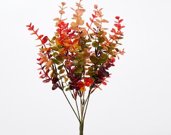 May include: A bunch of artificial eucalyptus stems with leaves in shades of red, orange, and green.