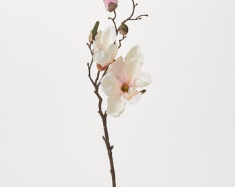 Puede incluir: Un solo tallo de flores de magnolia artificiales con dos flores abiertas y un capullo cerrado. Las flores son de un blanco suave con un toque de rosa en el centro. El tallo es marrón y tiene un aspecto natural.