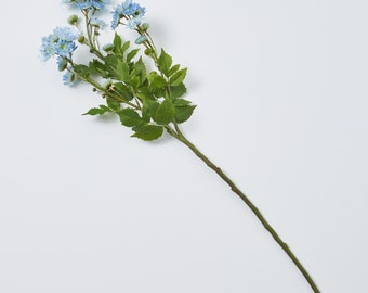 May include: A single stem of artificial flowers with light blue blossoms and green leaves. The stem is a dark brown color and the flowers are clustered together. The leaves are a vibrant green color. The flowers are a soft, muted blue.
