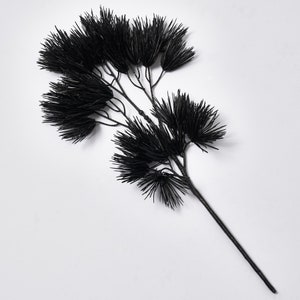 May include: A black artificial pine branch with multiple sprigs. The branch is long and slender with a dark brown stem.
