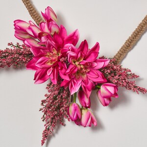May include: A pink floral wreath with pink flowers and greenery. The wreath is made of natural materials and is perfect for adding a touch of spring to your home.