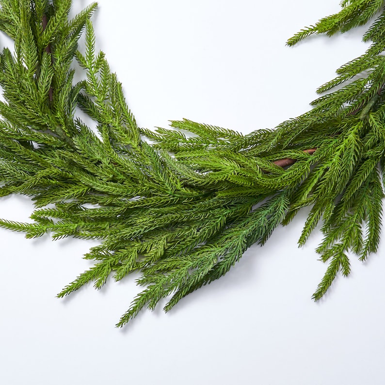 May include: A green artificial pine garland with long, thin needles. The garland is perfect for adding a touch of greenery to your home decor.