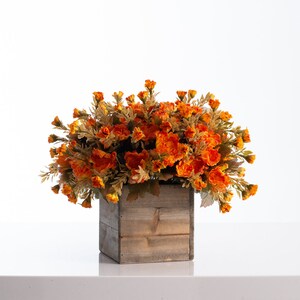 May include: A wooden box planter filled with a large arrangement of orange and yellow artificial flowers.