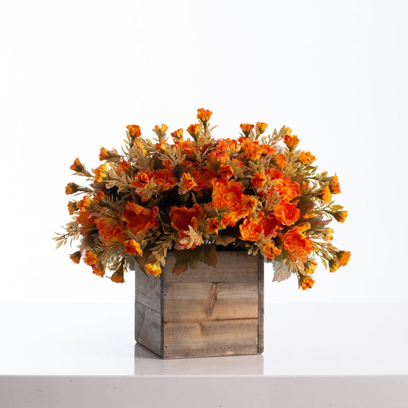May include: A wooden box planter filled with a large arrangement of orange and yellow artificial flowers.