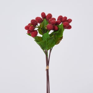 May include: A bundle of artificial berries with a vibrant red color and textured surface. The berries are clustered together with green leaves and brown stems, tied with twine. The background is plain white.