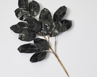 May include: A black artificial leaf sprig with a gold stem. The leaves are glossy and have a realistic texture.