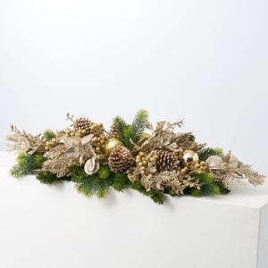 Pode incluir: Um centro de mesa de Natal dourado e verde com ramos de pinheiro, pinhas, bagas e ornamentos dourados.