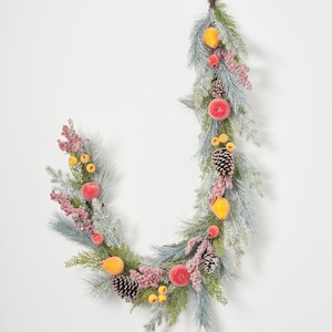 May include: A festive garland with frosted blue-green pine foliage, decorated with red and yellow fruit, pink berries, and pine cones. The garland is arranged in a crescent shape, suitable for seasonal decoration.