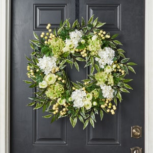 Peut inclure: Une couronne florale verte et blanche avec des hortensias blancs et des feuilles vertes. La couronne est d&eacute;cor&eacute;e de petites baies jaunes.