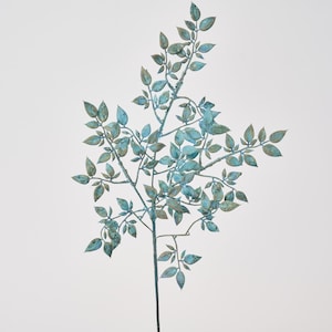 Può includere: Un ramo decorativo in metallo con foglie. Le foglie sono un mix di blu e verde, con una finitura anticata. Il ramo è un singolo stelo con più rami e foglie più piccoli.